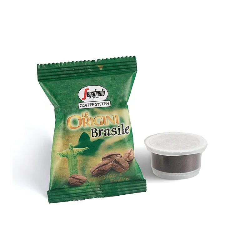 A Segafredo Zanetti® Coffee Espresso 1 Brewer pod next to a green and beige Segafredo Zanetti® Coffee “Brazilian Single Origin Espresso Single-Serve Cartridges” packet, which features a statue and coffee beans illustrated on the packaging, showcases the rich flavors of Brazilian Single Origin Espresso from the Nossa Senhora da Guia plantation.