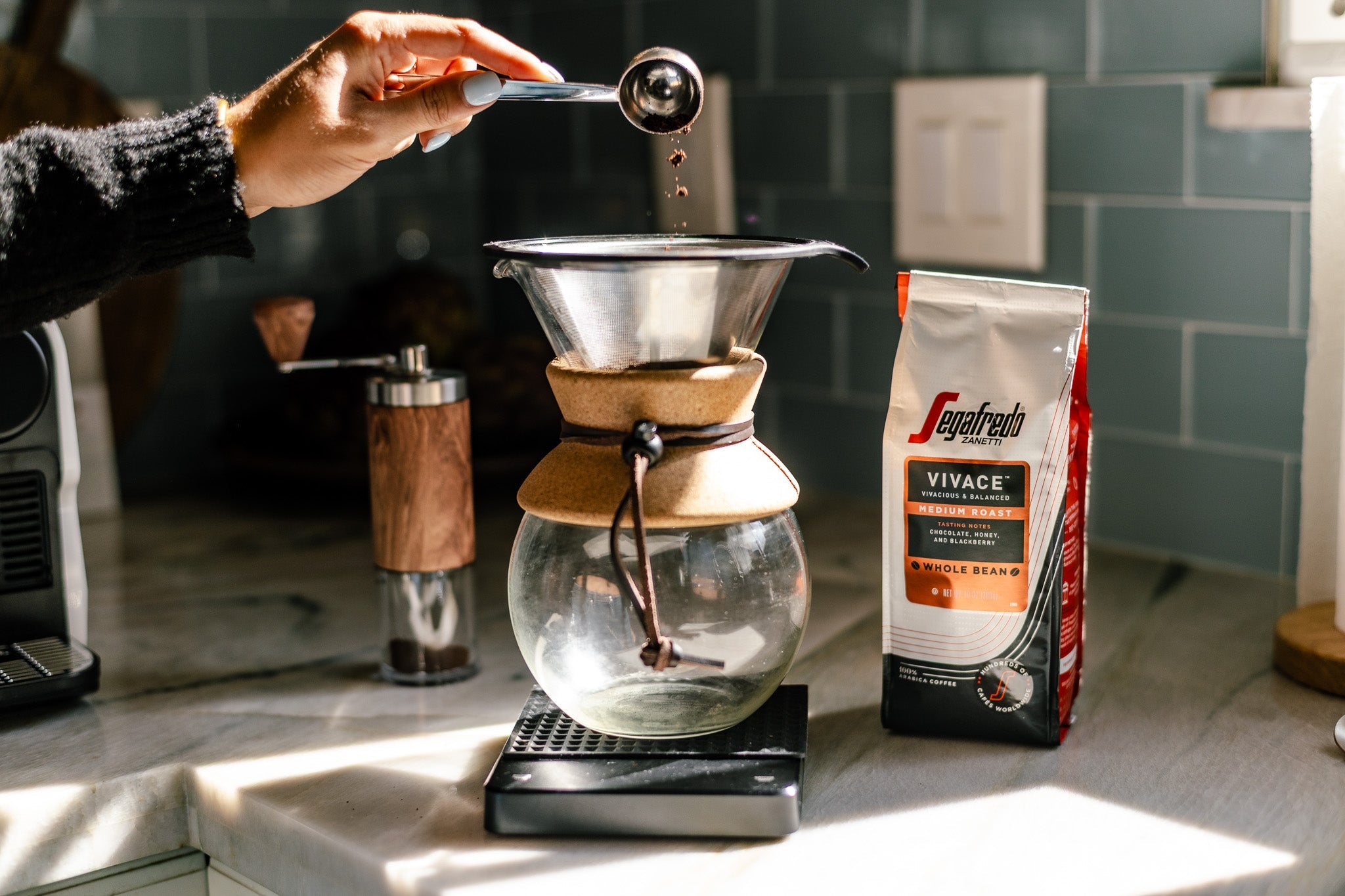 Person pours coffee from a Chemex into a mug, with a bag of Sagafredo Vivace coffee beans placed nearby on a countertop.