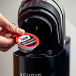 Load image into Gallery viewer, A hand placing a Segafredo Zanetti® Coffee Crescendo Medium Roast Keurig K-Cup® Pod in a Keurig coffee machine, capturing the essence of Italian coffee style with its low fruit tones.
